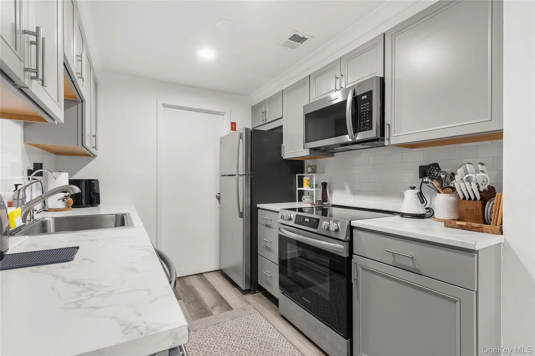 Kitchen featuring gray cabinets, appliances with stainless steel finishes, light countertops, tasteful backsplash, and light wood-type flooring Kitchen featuring gray cabinets, appliances with stainless steel finishes, light countertops, tasteful backsplash, and light wood-type flooring