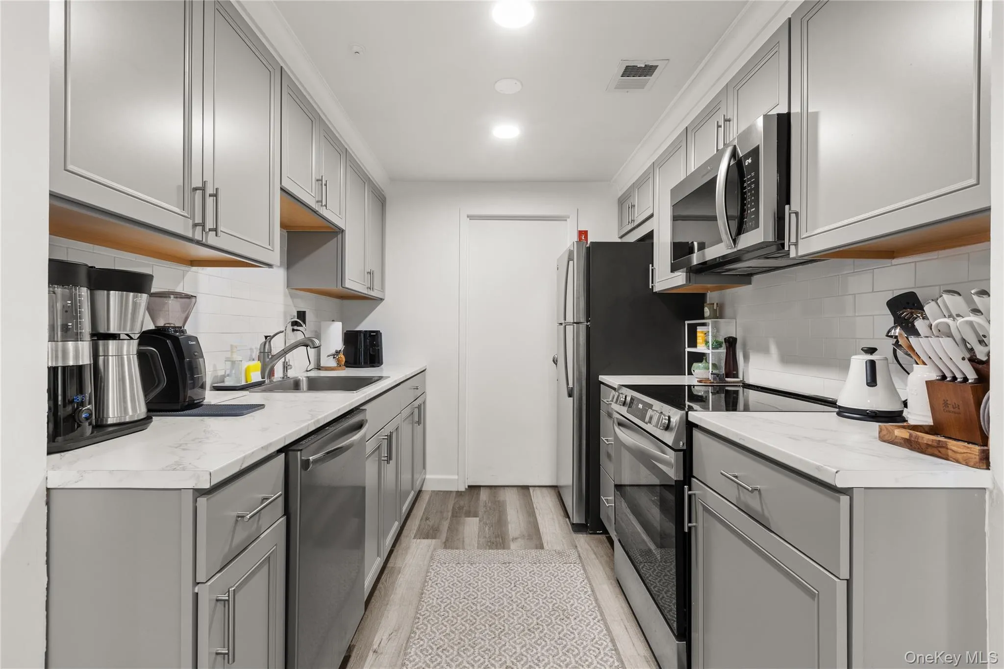 Kitchen with gray cabinetry, stainless steel appliances, light wood-type flooring, and decorative backsplash Kitchen with gray cabinetry, stainless steel appliances, light wood-type flooring, and decorative backsplash