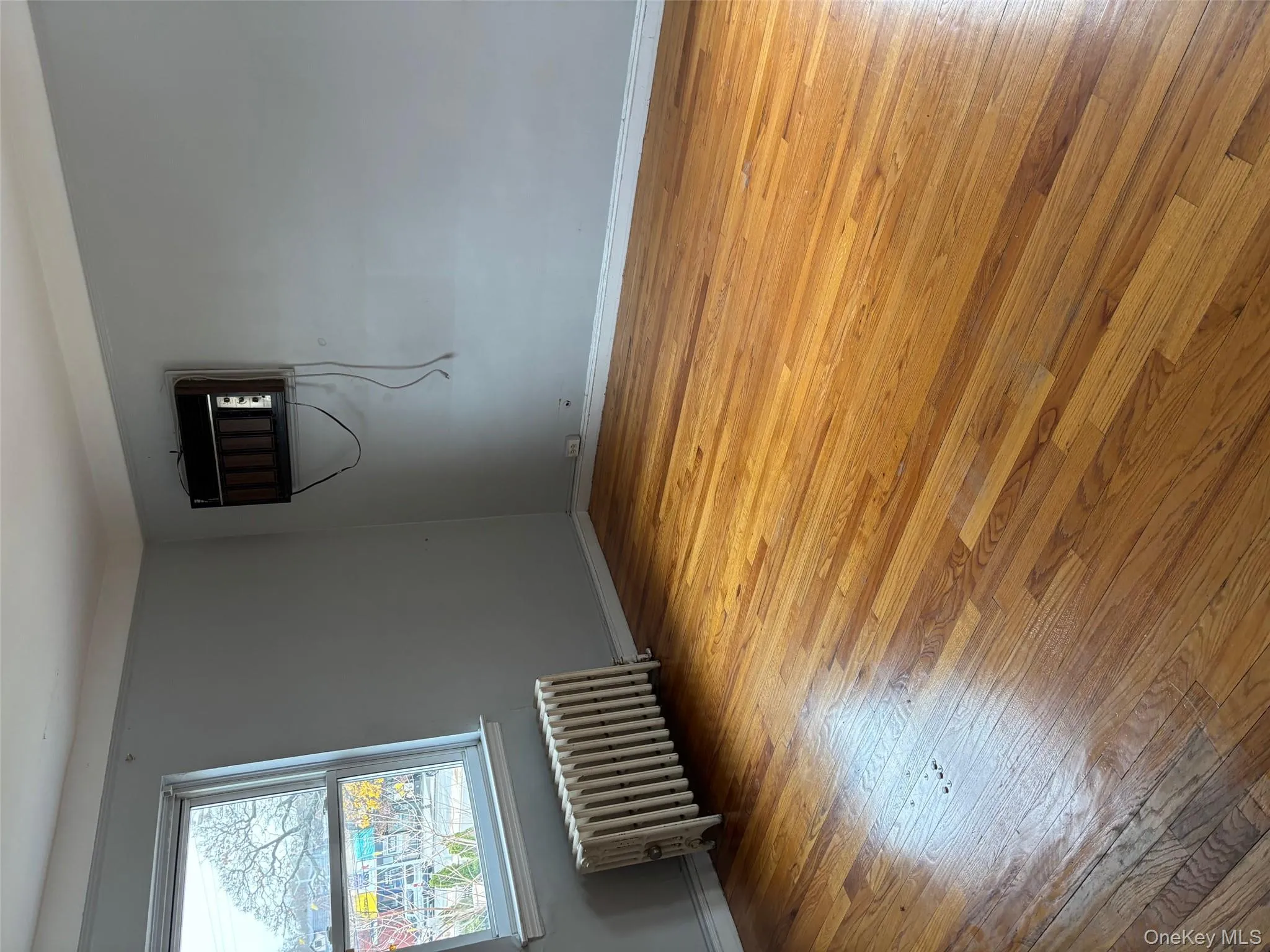 Unfurnished room with radiator, light wood-style flooring, and a wall mounted AC Unfurnished room with radiator, light wood-style flooring, and a wall mounted AC