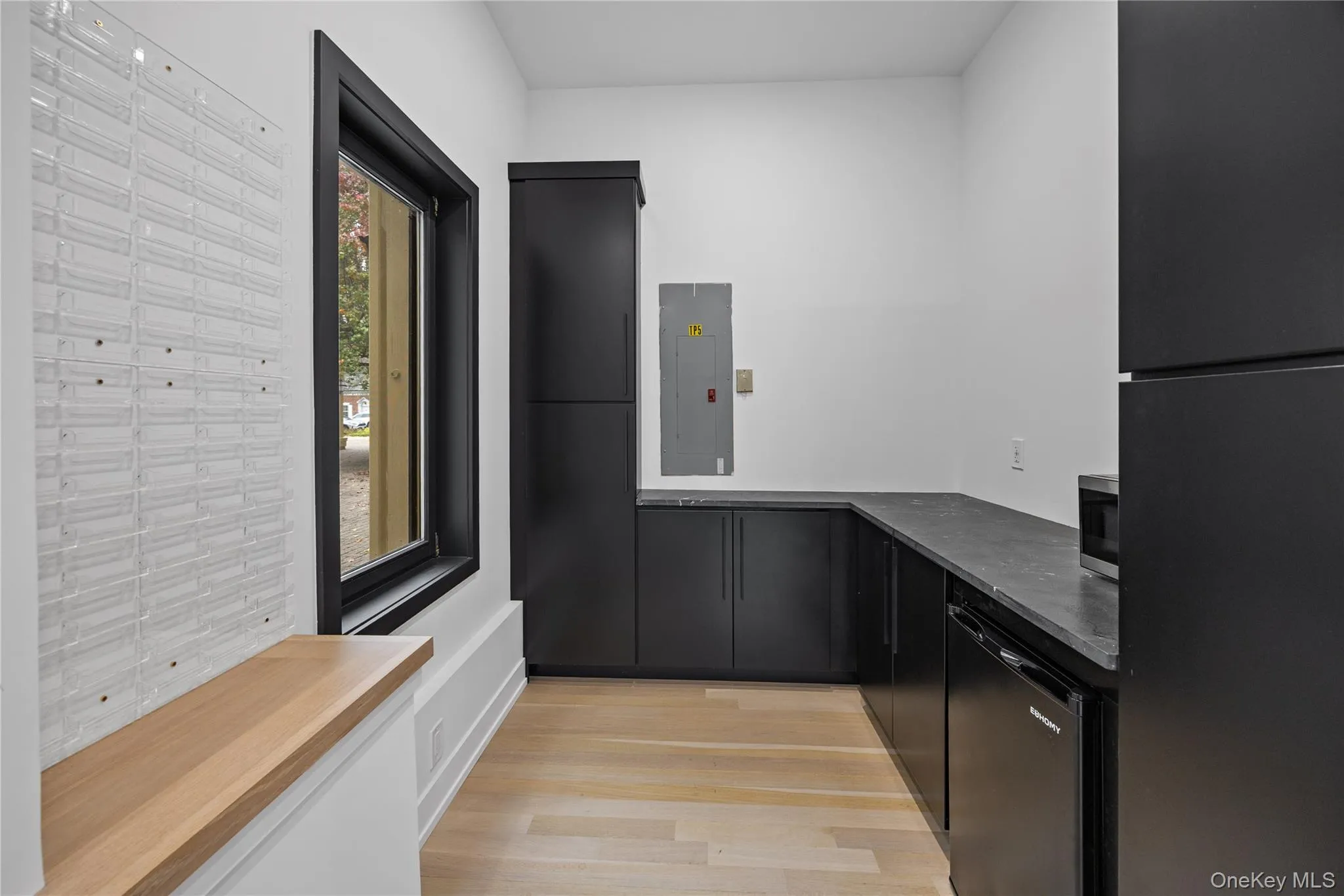 Kitchen featuring freestanding refrigerator, dark cabinets, dishwashing machine, electric panel, and light wood-type flooring Kitchen featuring freestanding refrigerator, dark cabinets, dishwashing machine, electric panel, and light wood-type flooring