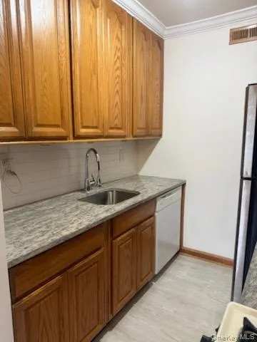 Kitchen with brown cabinets, light stone counters, ornamental molding, freestanding refrigerator, and tasteful backsplash Kitchen with brown cabinets, light stone counters, ornamental molding, freestanding refrigerator, and tasteful backsplash