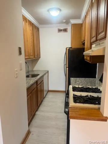 Kitchen featuring white appliances, brown cabinets, crown molding, under cabinet range hood, and light wood-style floors Kitchen featuring white appliances, brown cabinets, crown molding, under cabinet range hood, and light wood-style floors