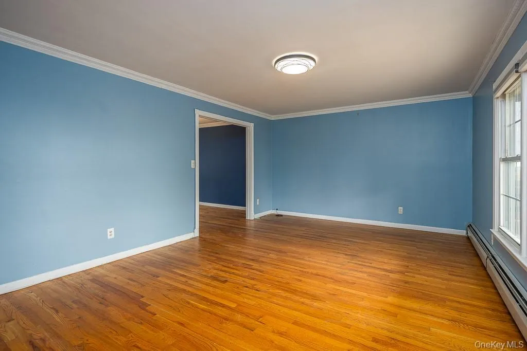 Unfurnished room with a baseboard heating unit, light wood-style flooring, and ornamental molding Unfurnished room with a baseboard heating unit, light wood-style flooring, and ornamental molding