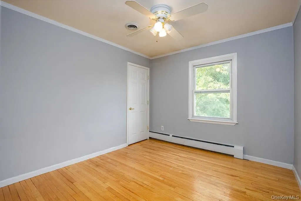 Spare room featuring baseboard heating, crown molding, light wood-type flooring, and ceiling fan Spare room featuring baseboard heating, crown molding, light wood-type flooring, and ceiling fan