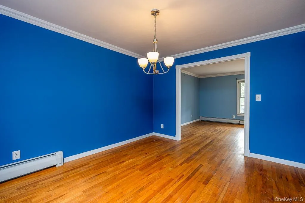 Empty room featuring ornamental molding, a chandelier, hardwood / wood-style flooring, a baseboard radiator, and baseboard heating Empty room featuring ornamental molding, a chandelier, hardwood / wood-style flooring, a baseboard radiator, and baseboard heating