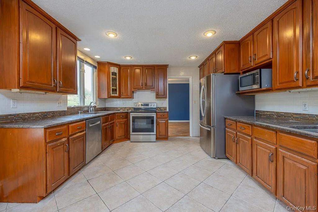 Kitchen featuring brown cabinets, stainless steel appliances, recessed lighting, glass insert cabinets, and dark stone counters Kitchen featuring brown cabinets, stainless steel appliances, recessed lighting, glass insert cabinets, and dark stone counters
