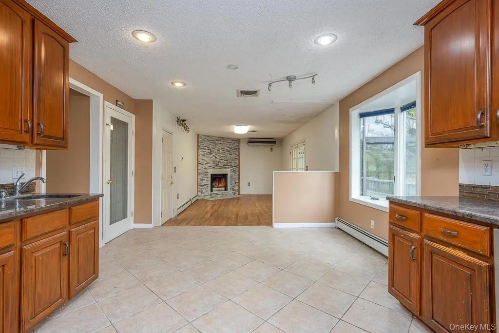Kitchen featuring brown cabinetry, decorative backsplash, dark stone counters, a textured ceiling, and a baseboard heating unit Kitchen featuring brown cabinetry, decorative backsplash, dark stone counters, a textured ceiling, and a baseboard heating unit