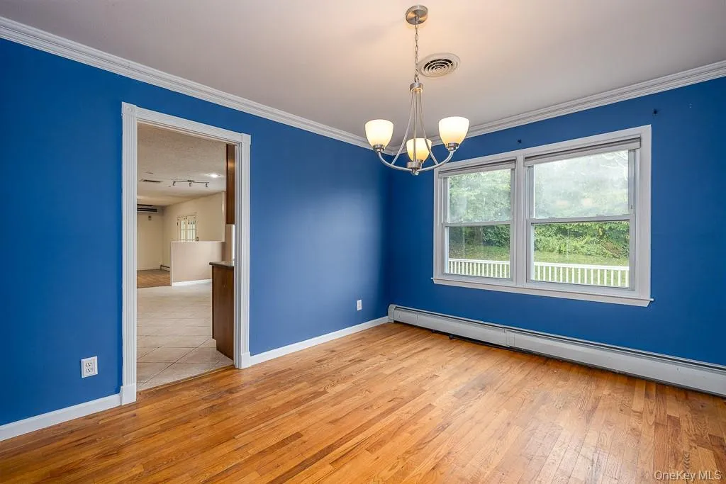 Empty room featuring a chandelier, a baseboard radiator, crown molding, and light wood-style flooring Empty room featuring a chandelier, a baseboard radiator, crown molding, and light wood-style flooring