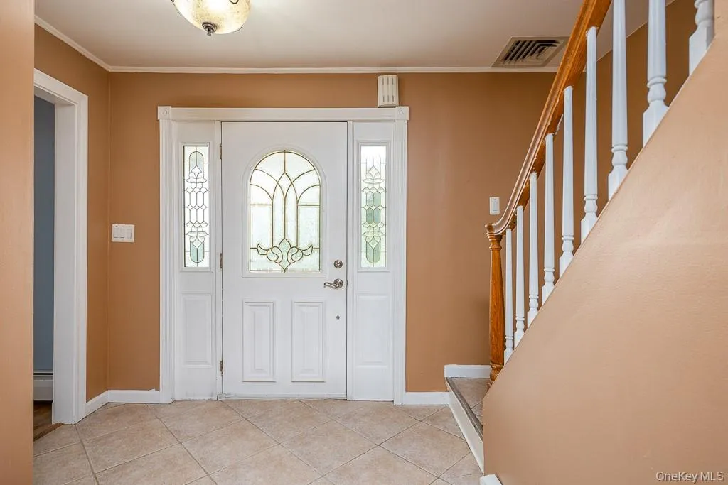 Foyer entrance with light tile patterned floors, crown molding, stairs, and baseboard heating Foyer entrance with light tile patterned floors, crown molding, stairs, and baseboard heating