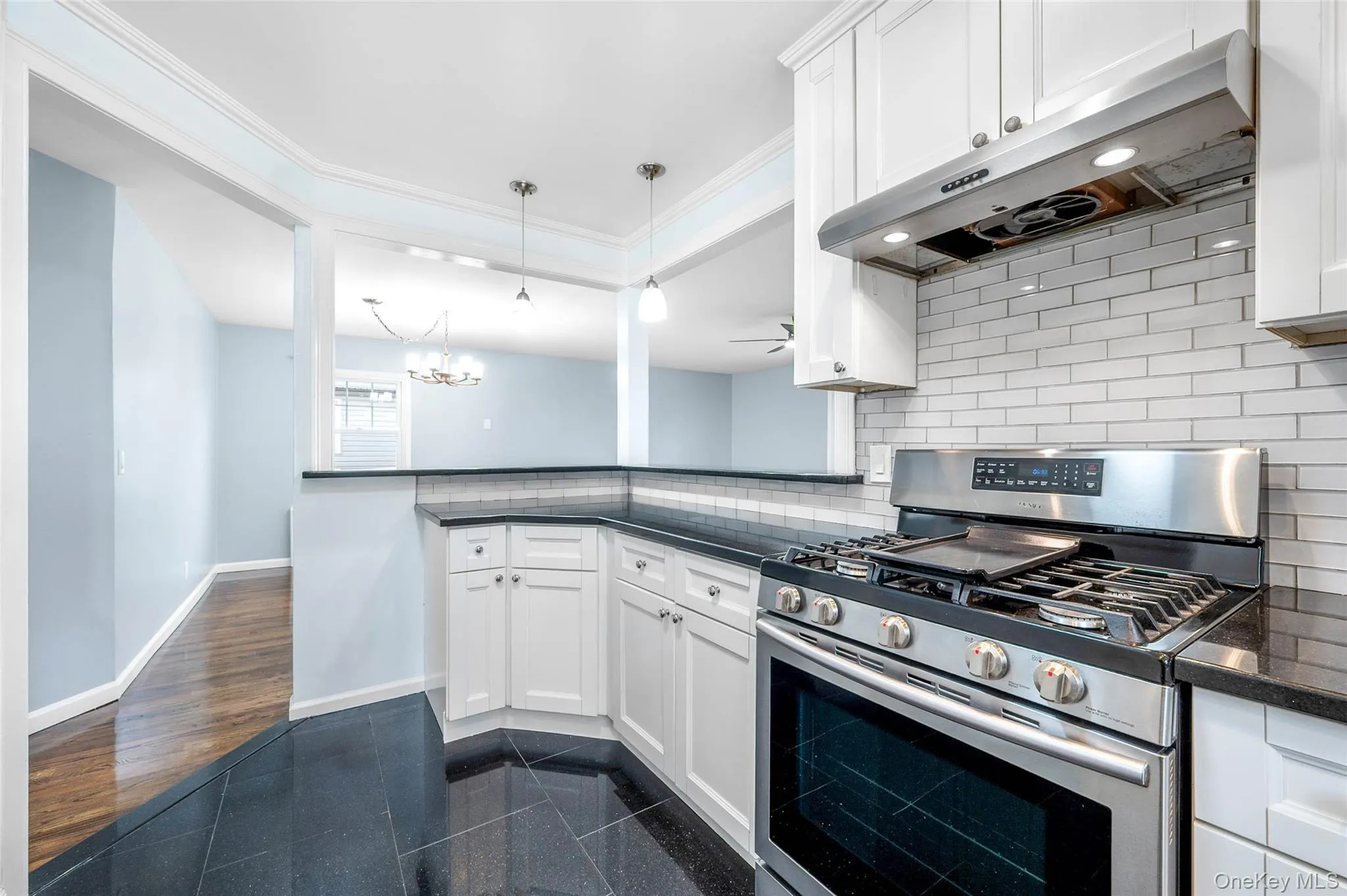 Kitchen featuring stainless steel gas range oven, white cabinets, under cabinet range hood, granite tiled floors, and pendant lighting Kitchen featuring stainless steel gas range oven, white cabinets, under cabinet range hood, granite tiled floors, and pendant lighting