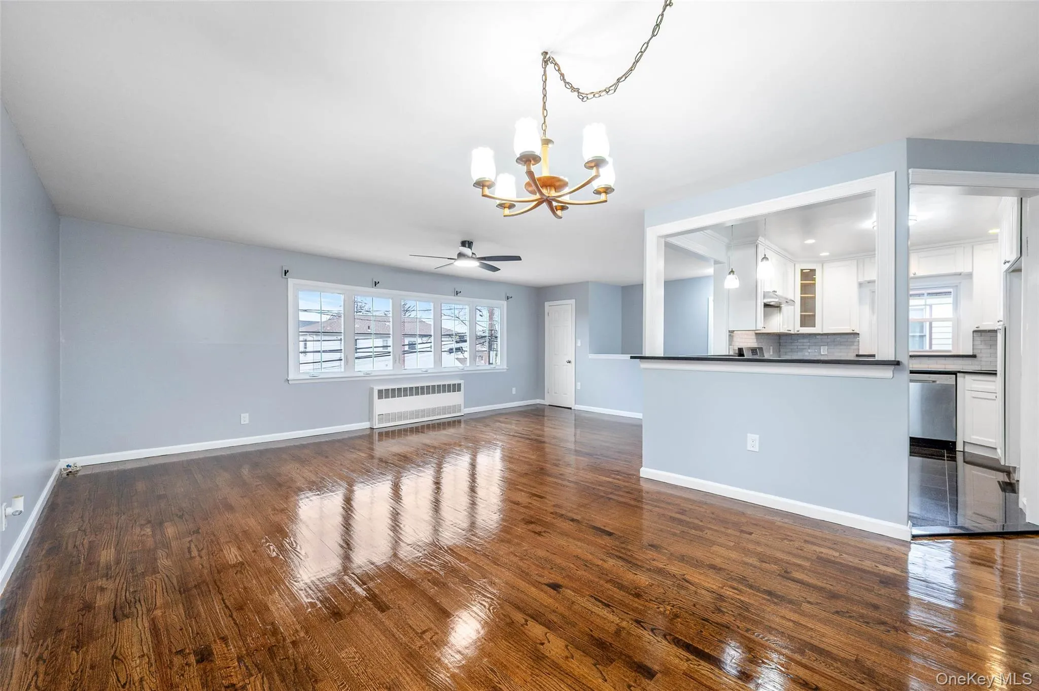 Unfurnished living room featuring a chandelier, dark wood finished floors, a ceiling fan, and radiator heating unit Unfurnished living room featuring a chandelier, dark wood finished floors, a ceiling fan, and radiator heating unit