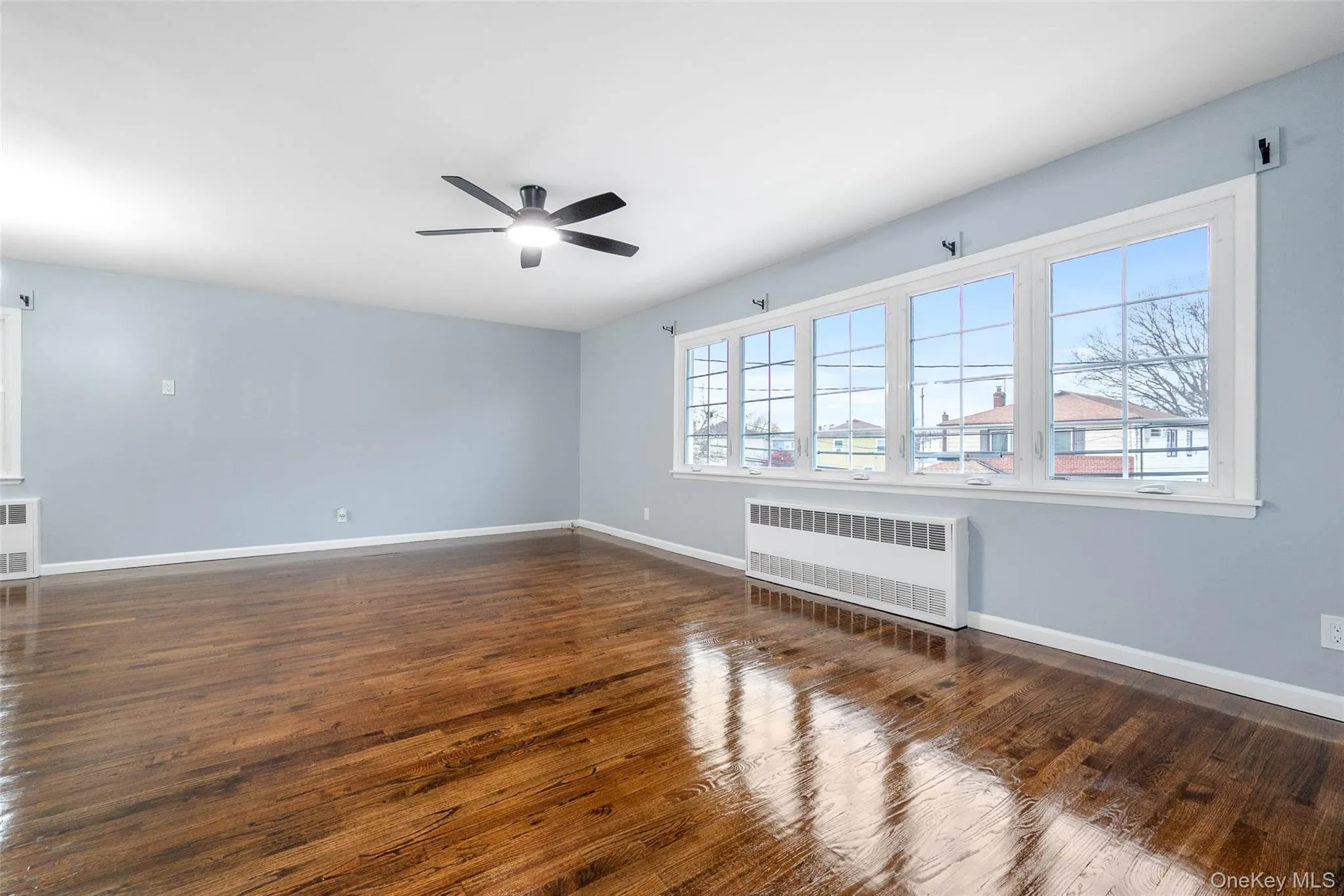 Unfurnished room featuring radiator heating unit, dark wood finished floors, and a ceiling fan Unfurnished room featuring radiator heating unit, dark wood finished floors, and a ceiling fan