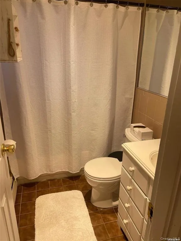 Bathroom with vanity, curtained shower, dark tile patterned floors, and tile walls Bathroom with vanity, curtained shower, dark tile patterned floors, and tile walls