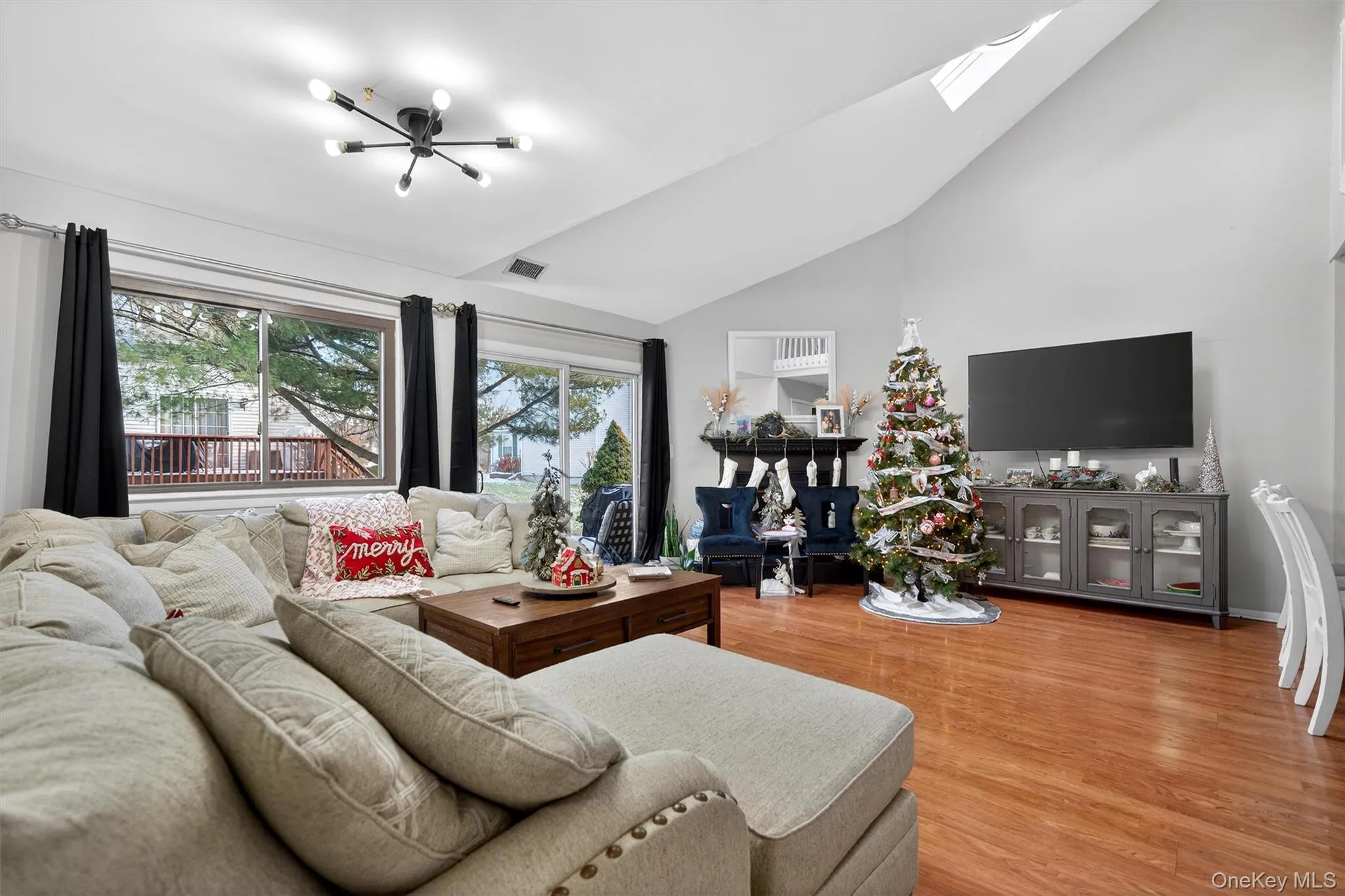 Living area with light wood-style floors, high vaulted ceiling, a skylight, and a chandelier Living area with light wood-style floors, high vaulted ceiling, a skylight, and a chandelier
