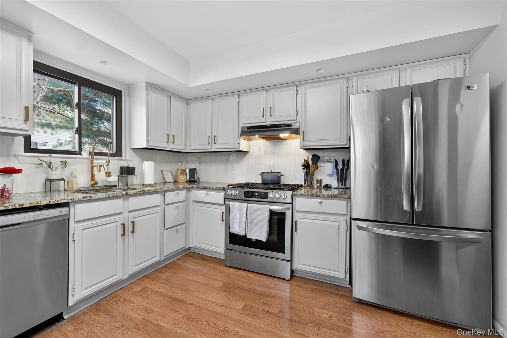 Kitchen featuring stainless steel appliances, light stone countertops, white cabinetry, light wood-type flooring, and decorative backsplash Kitchen featuring stainless steel appliances, light stone countertops, white cabinetry, light wood-type flooring, and decorative backsplash