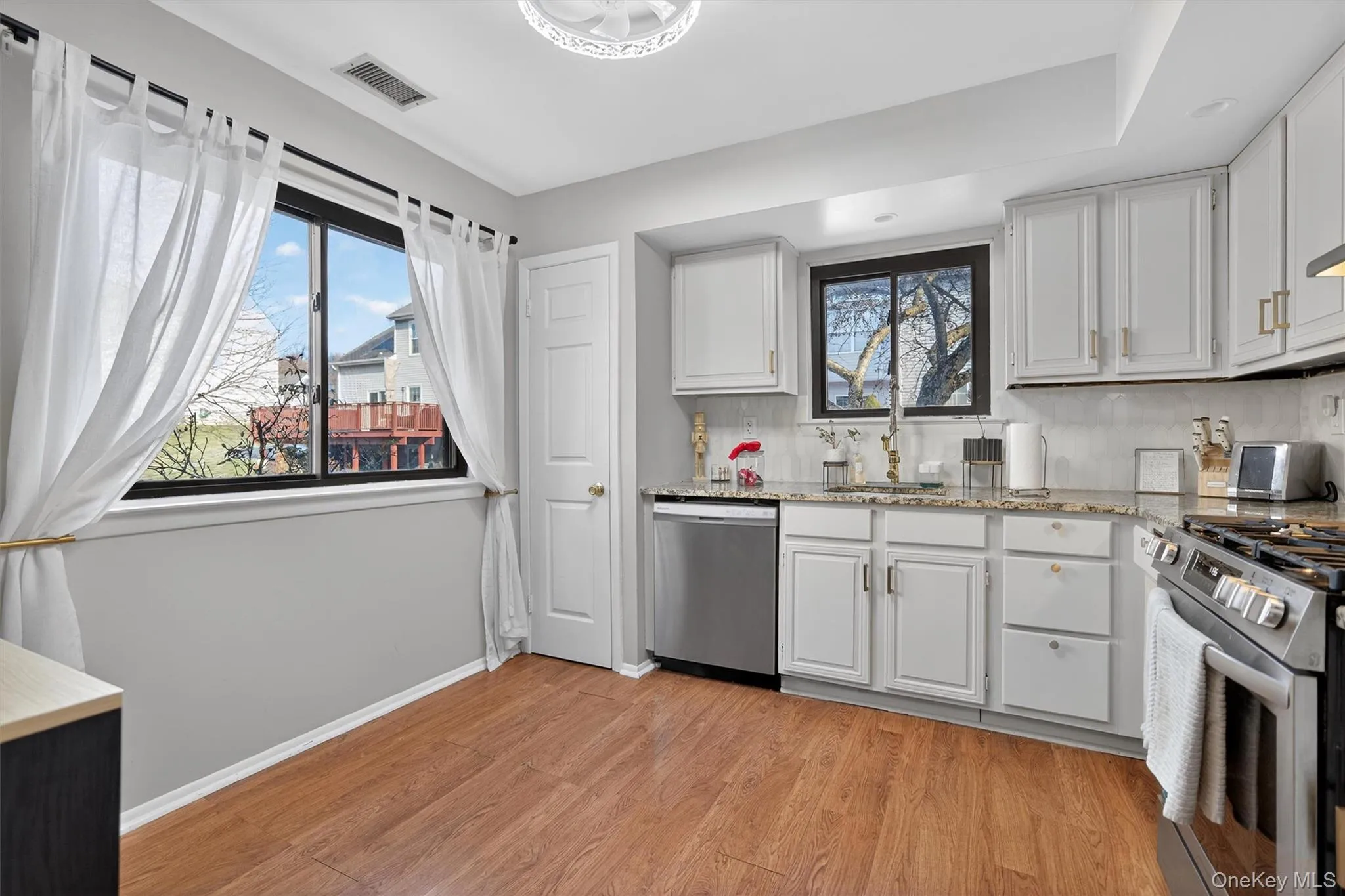 Kitchen with light stone counters, white cabinetry, stainless steel appliances, and decorative backsplash Kitchen with light stone counters, white cabinetry, stainless steel appliances, and decorative backsplash