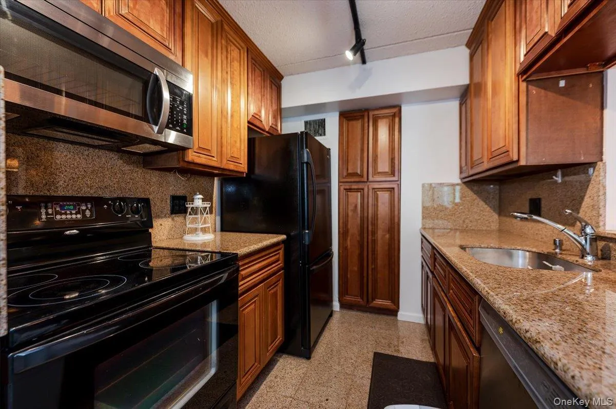 Kitchen featuring black appliances, backsplash, light stone counters, brown cabinets, and a textured ceiling Kitchen featuring black appliances, backsplash, light stone counters, brown cabinets, and a textured ceiling