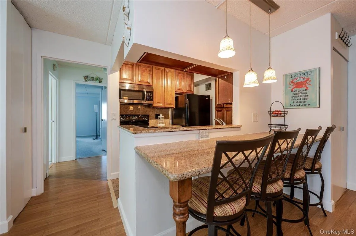 Kitchen featuring brown cabinets, decorative light fixtures, black appliances, light wood-type flooring, and a kitchen breakfast bar Kitchen featuring brown cabinets, decorative light fixtures, black appliances, light wood-type flooring, and a kitchen breakfast bar