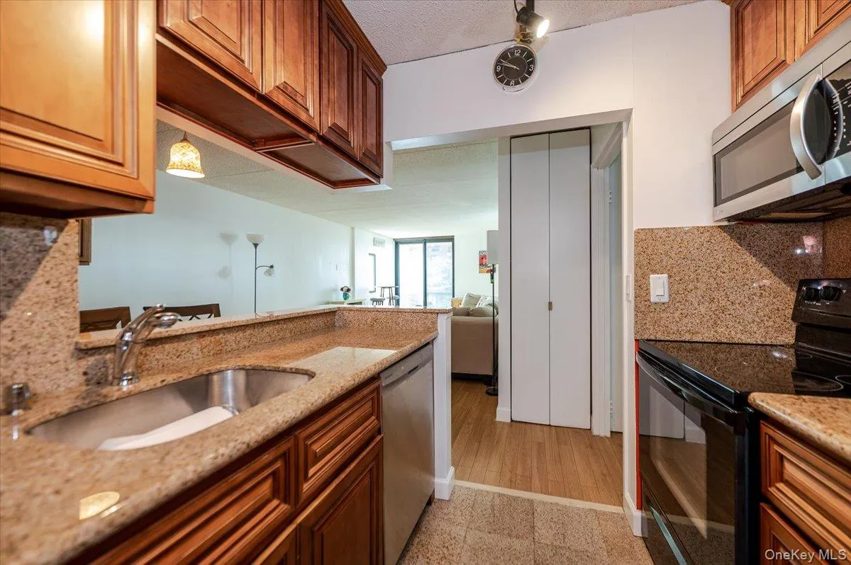 Kitchen with appliances with stainless steel finishes, backsplash, light stone countertops, brown cabinets, and a textured ceiling Kitchen with appliances with stainless steel finishes, backsplash, light stone countertops, brown cabinets, and a textured ceiling