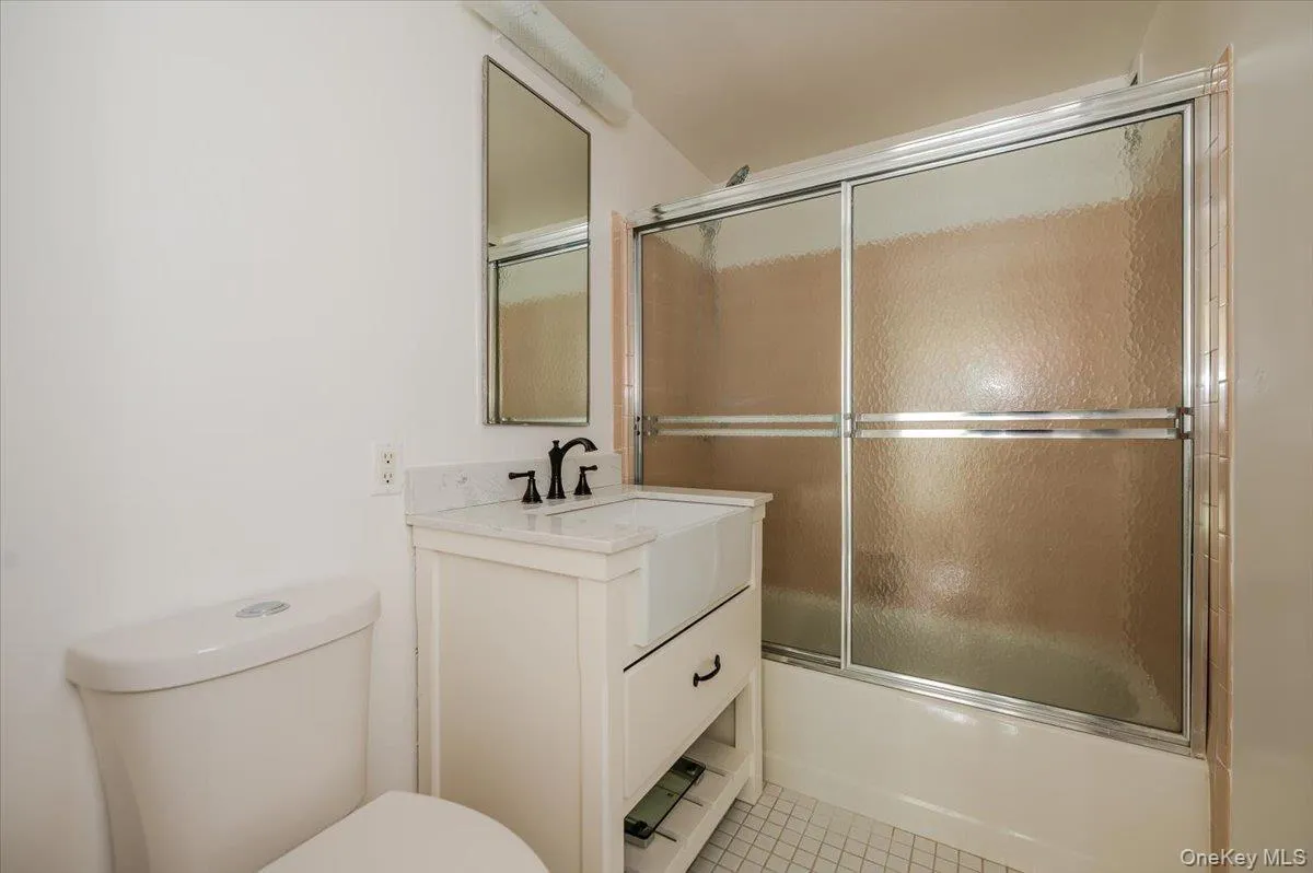 Full bath with enclosed tub / shower combo, vanity, and light tile patterned floors Full bath with enclosed tub / shower combo, vanity, and light tile patterned floors