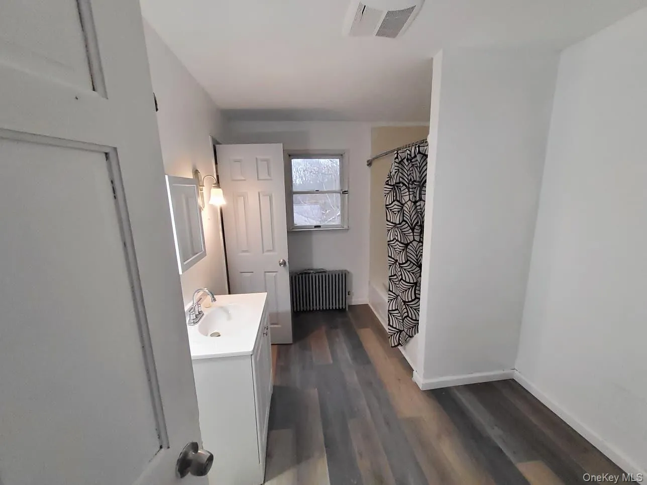 Full bath featuring vanity, radiator, dark wood finished floors, and shower / tub combo Full bath featuring vanity, radiator, dark wood finished floors, and shower / tub combo