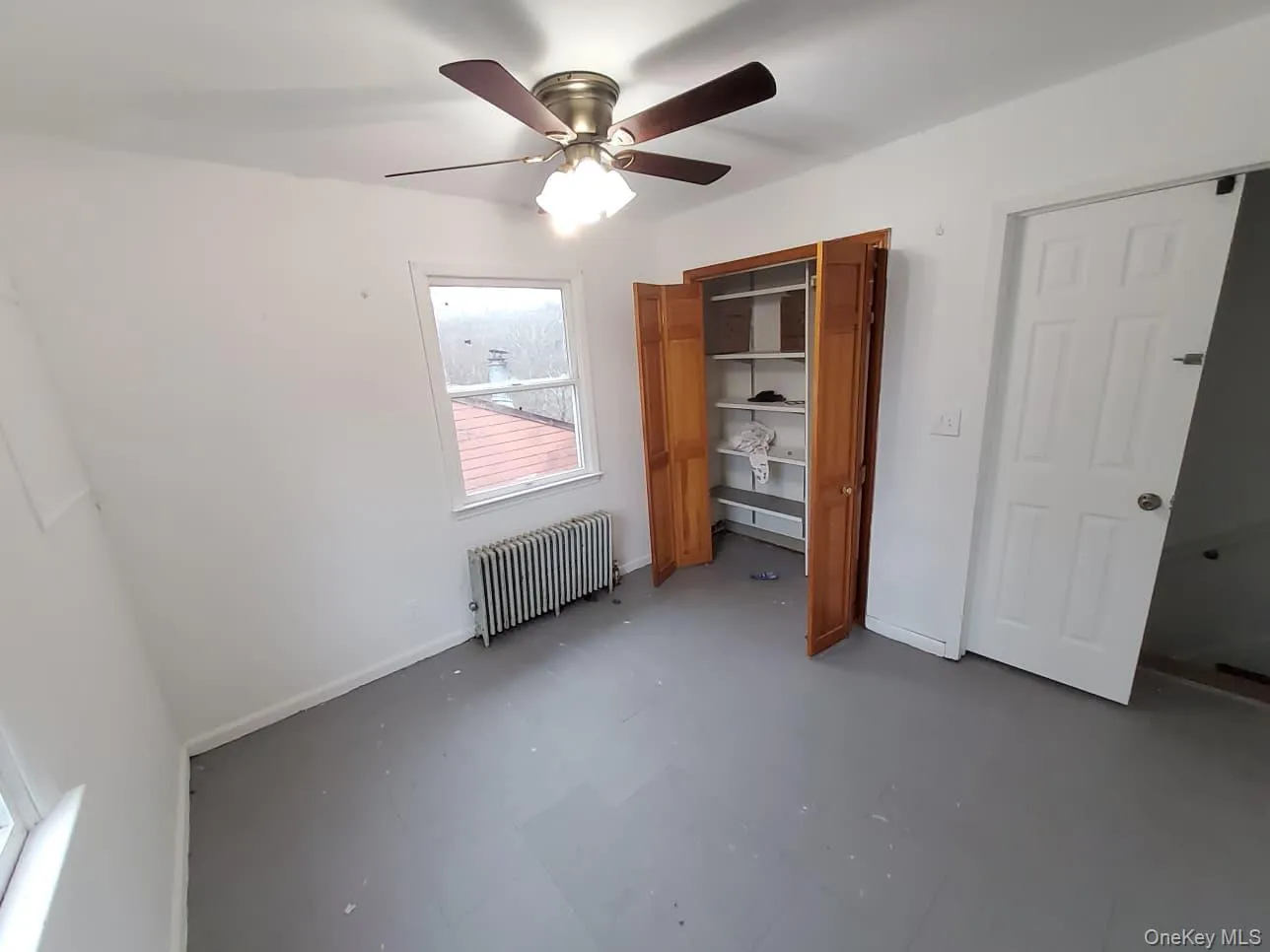 Unfurnished bedroom featuring radiator heating unit, ceiling fan, and concrete flooring Unfurnished bedroom featuring radiator heating unit, ceiling fan, and concrete flooring