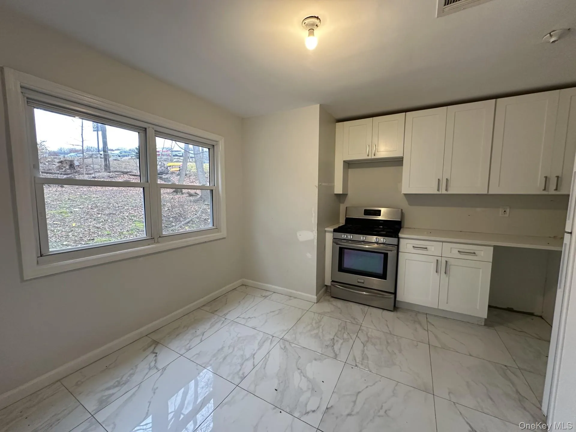 Kitchen with gas stove, light marble finish flooring, white cabinetry, and freestanding refrigerator Kitchen with gas stove, light marble finish flooring, white cabinetry, and freestanding refrigerator