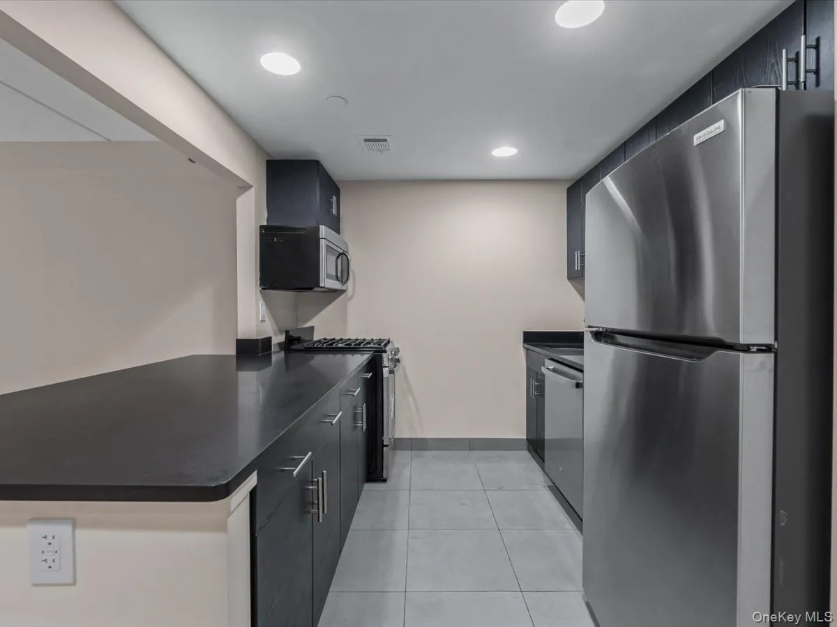 Kitchen with stainless steel appliances, dark cabinetry, recessed lighting, light tile patterned floors, and modern cabinets Kitchen with stainless steel appliances, dark cabinetry, recessed lighting, light tile patterned floors, and modern cabinets