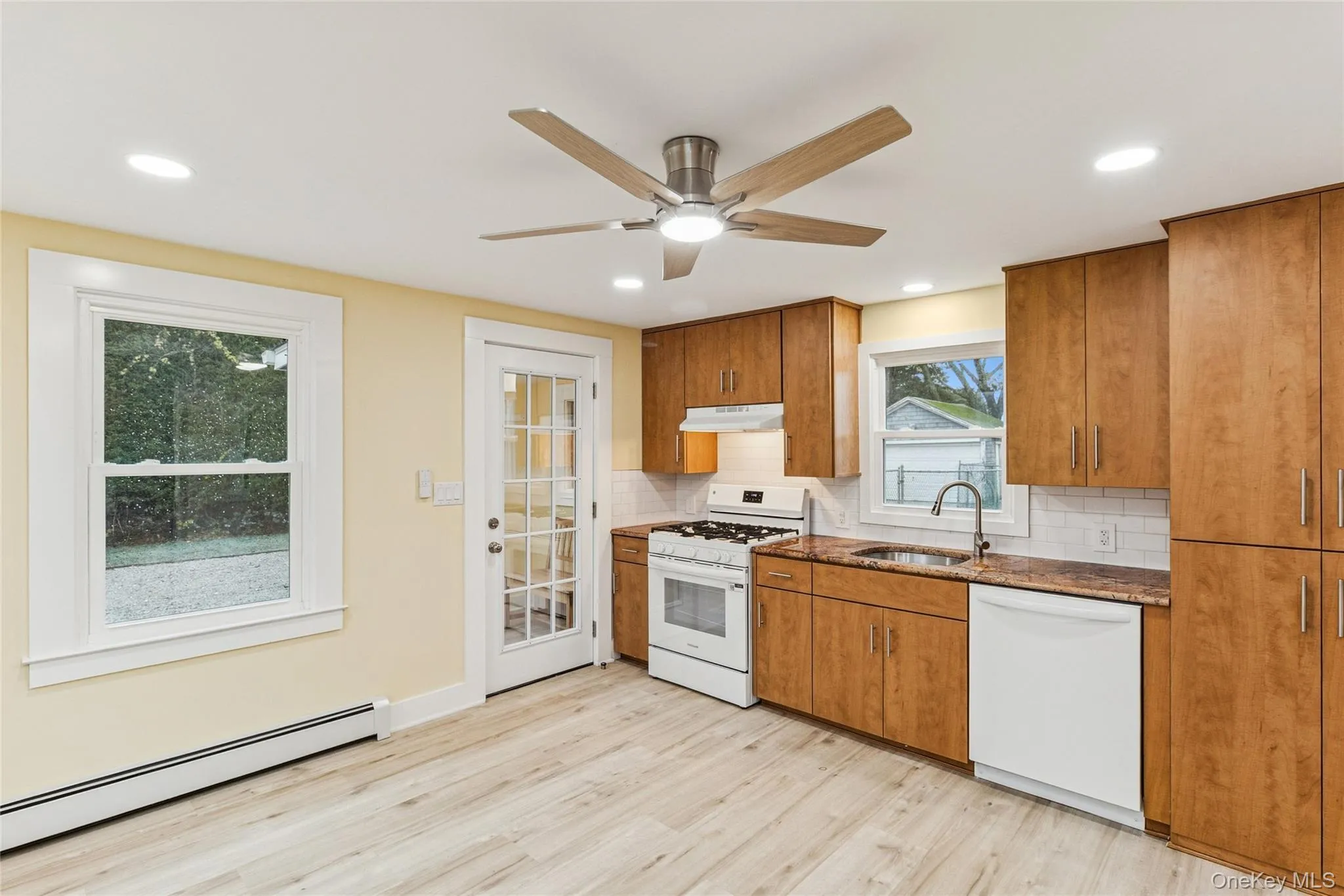 Kitchen with white appliances, brown cabinetry, a baseboard heating unit, decorative backsplash, and dark stone countertops Kitchen with white appliances, brown cabinetry, a baseboard heating unit, decorative backsplash, and dark stone countertops