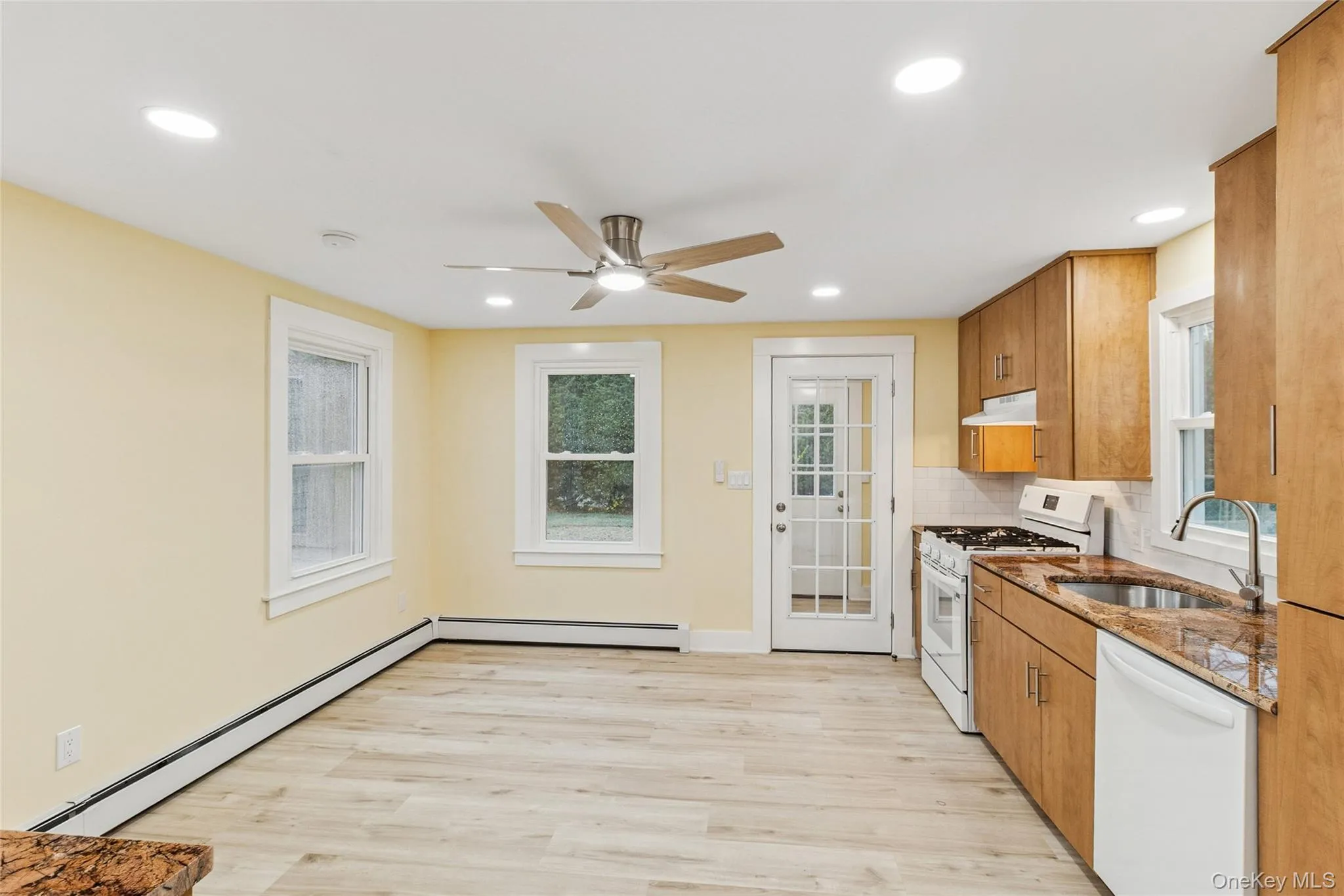 Kitchen featuring dark stone counters, baseboard heating, white appliances, brown cabinets, and recessed lighting Kitchen featuring dark stone counters, baseboard heating, white appliances, brown cabinets, and recessed lighting