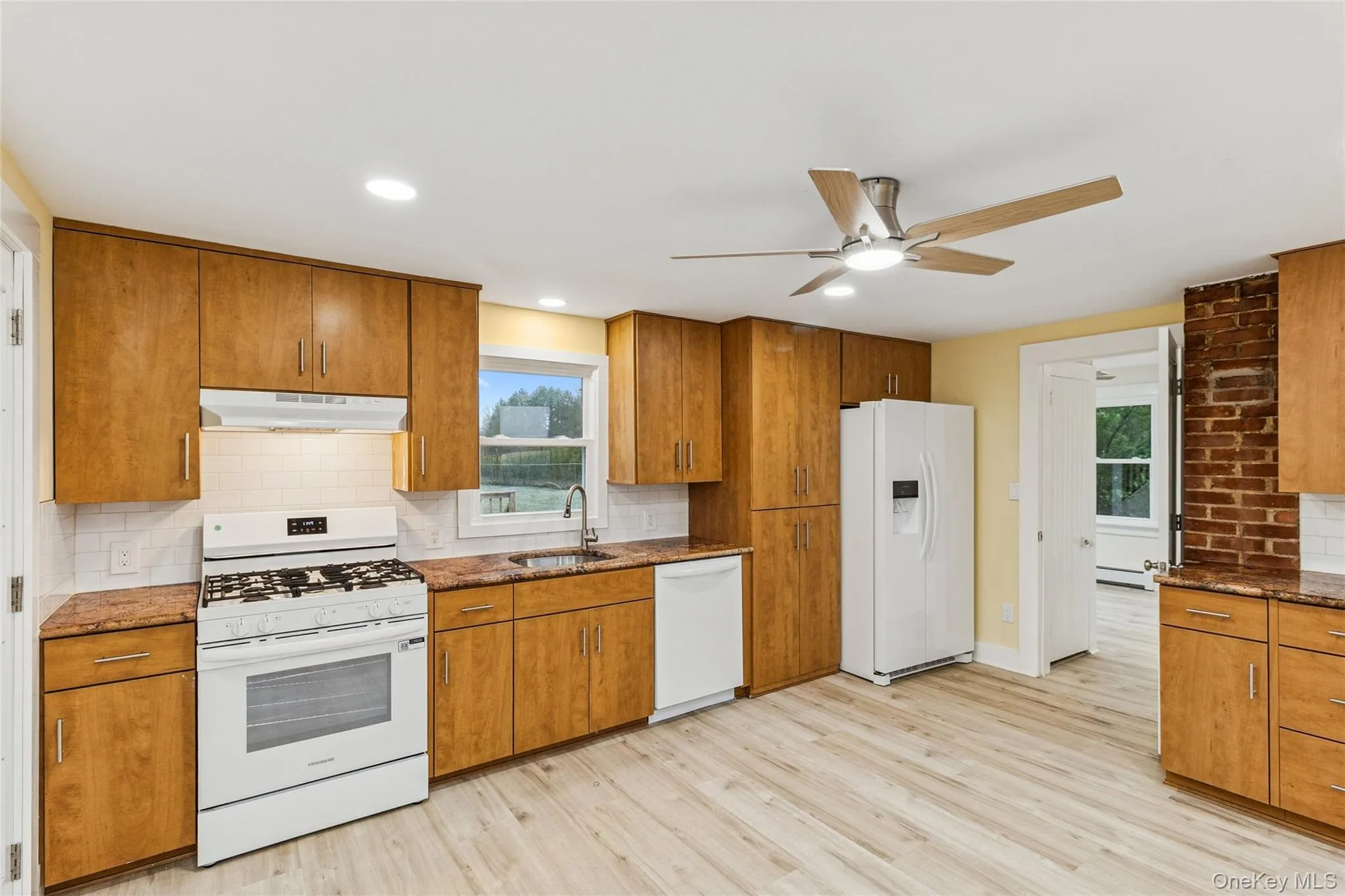 Kitchen with brown cabinetry, white appliances, dark stone countertops, backsplash, and recessed lighting Kitchen with brown cabinetry, white appliances, dark stone countertops, backsplash, and recessed lighting