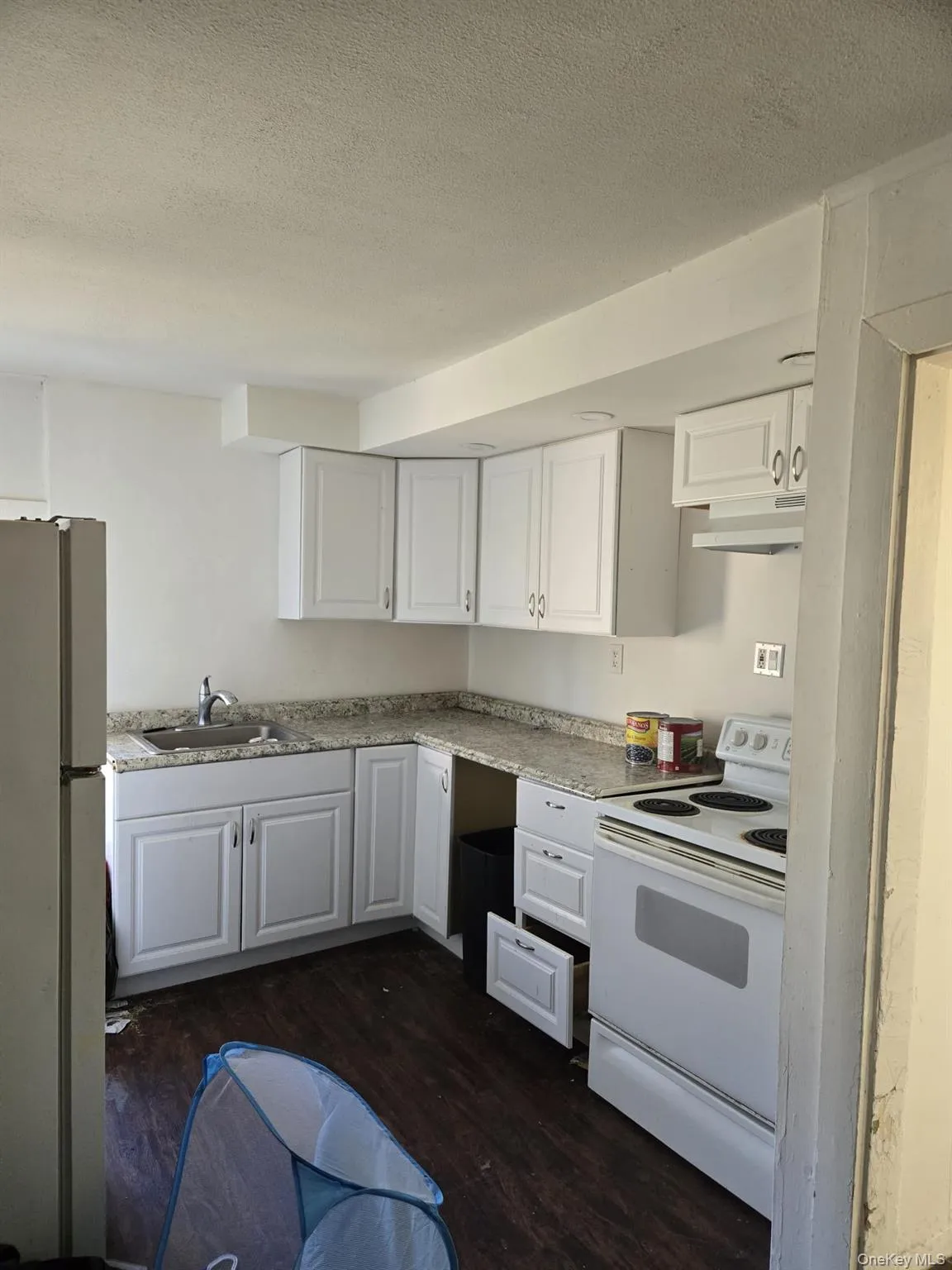 Kitchen with white appliances, white cabinetry, dark wood finished floors, a textured ceiling, and under cabinet range hood Kitchen with white appliances, white cabinetry, dark wood finished floors, a textured ceiling, and under cabinet range hood