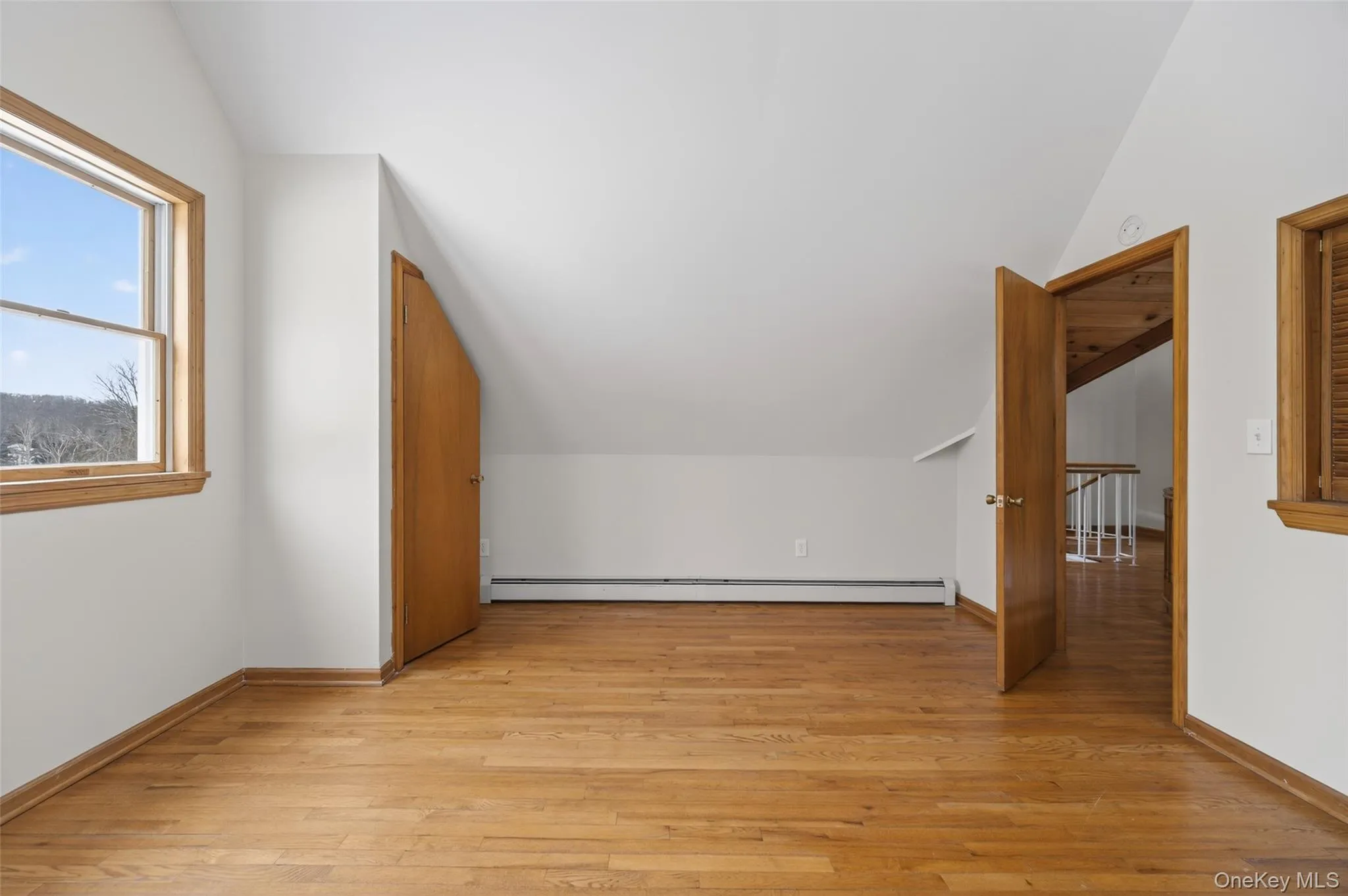 Bedroom featuring vaulted ceiling, light wood-type flooring, and a baseboard heating unit Bedroom featuring vaulted ceiling, light wood-type flooring, and a baseboard heating unit