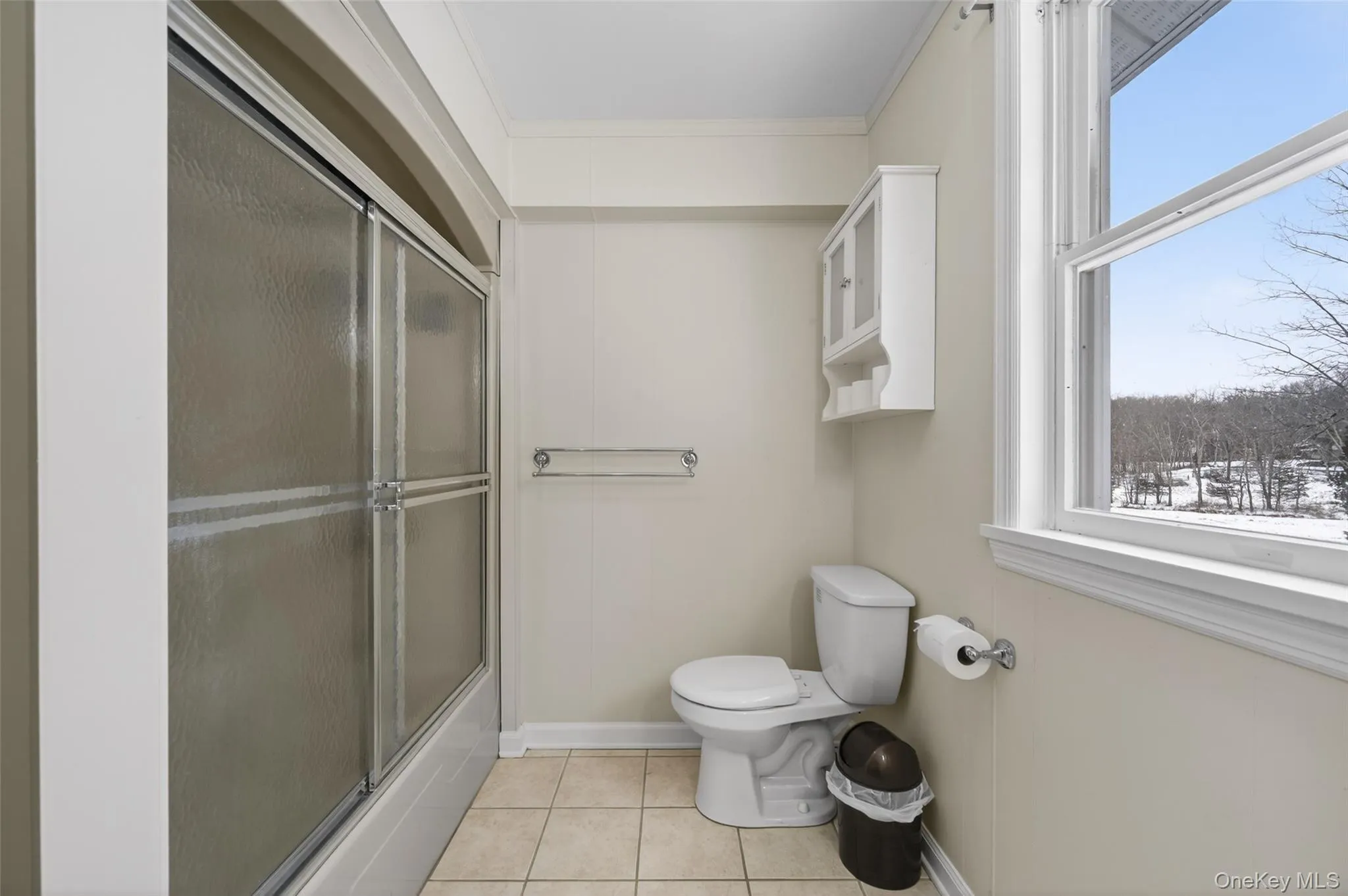 Full bathroom featuring light tile patterned floors, bath / shower combo with glass door, and ornamental molding Full bathroom featuring light tile patterned floors, bath / shower combo with glass door, and ornamental molding