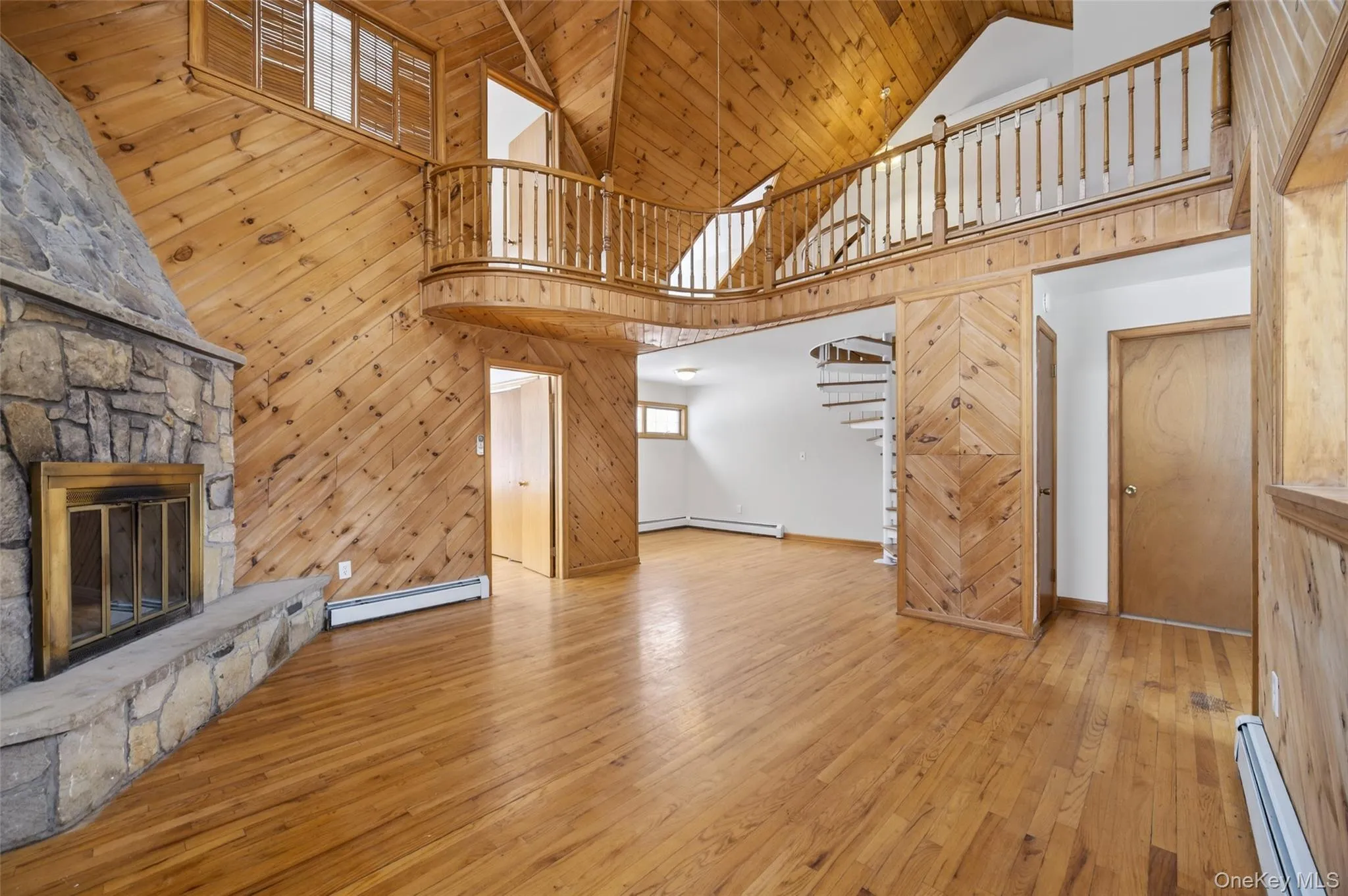 Unfurnished living room featuring wooden walls, a stone fireplace, a baseboard radiator, light wood finished floors, and high vaulted ceiling Unfurnished living room featuring wooden walls, a stone fireplace, a baseboard radiator, light wood finished floors, and high vaulted ceiling