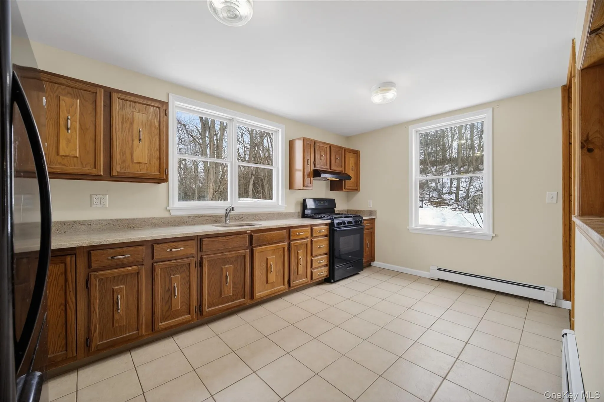Kitchen featuring black appliances, brown cabinetry, a baseboard radiator, and light countertops Kitchen featuring black appliances, brown cabinetry, a baseboard radiator, and light countertops