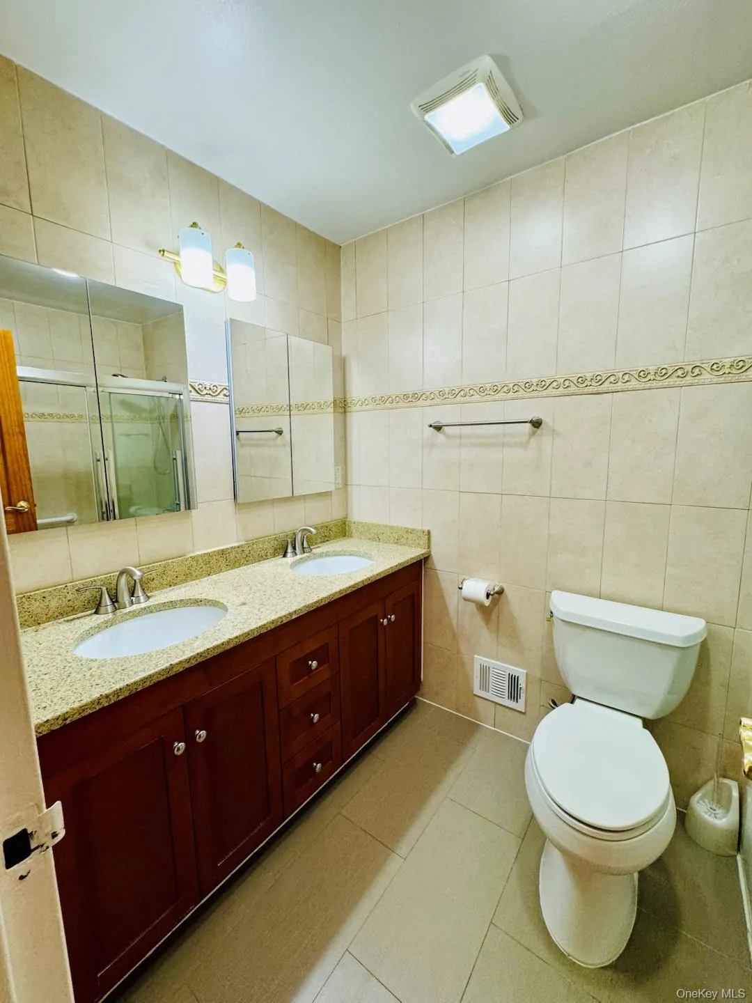 Full bath with tile walls, double vanity, a stall shower, and light tile patterned floors Full bath with tile walls, double vanity, a stall shower, and light tile patterned floors