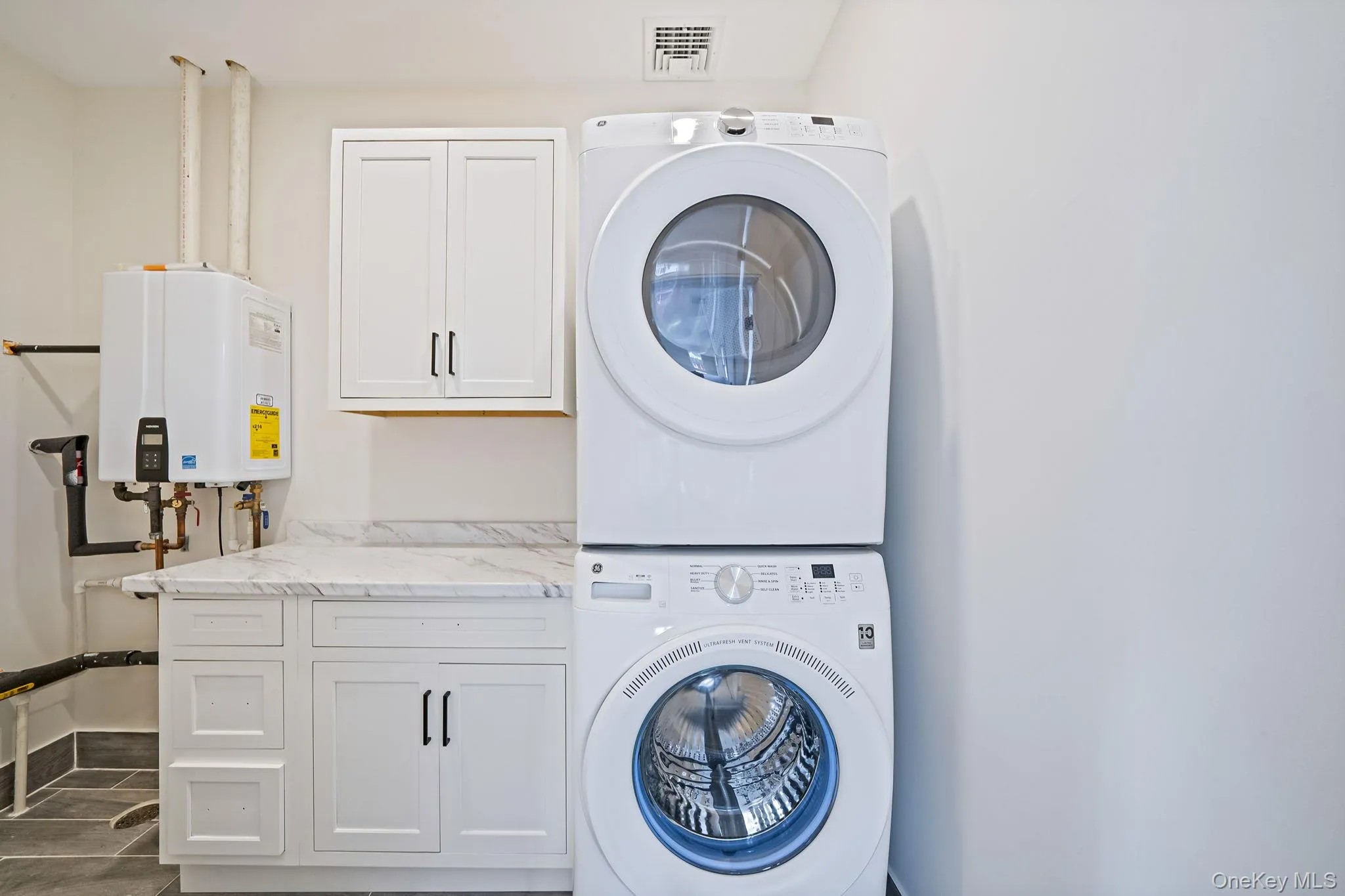Laundry area with cabinet space, stacked washer / drying machine, and tankless water heater Laundry area with cabinet space, stacked washer / drying machine, and tankless water heater