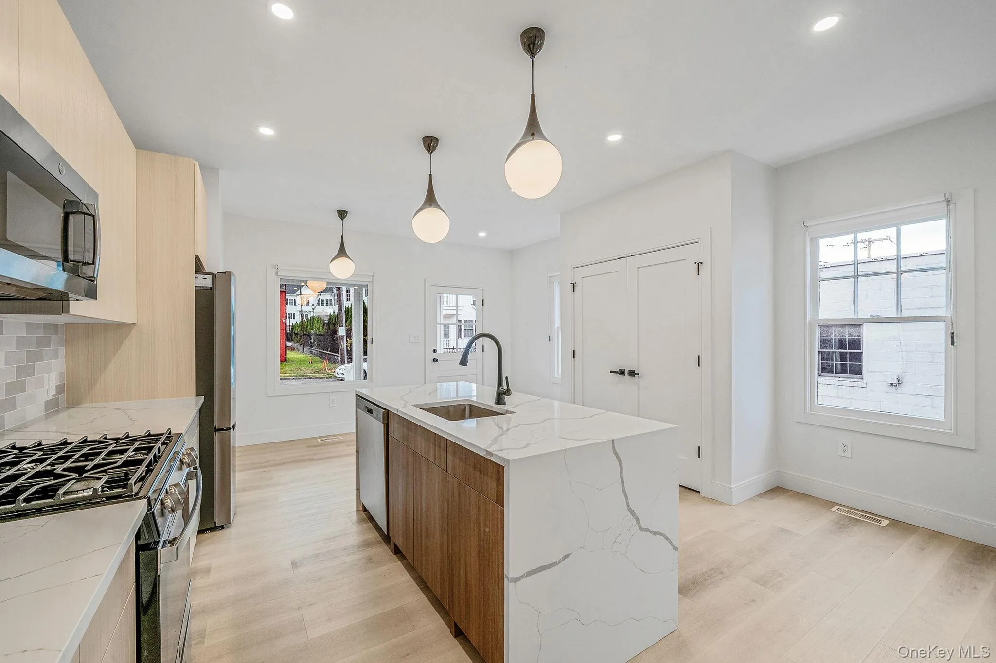 Kitchen featuring modern cabinets, decorative light fixtures, light stone counters, light wood-style flooring, and stainless steel appliances Kitchen featuring modern cabinets, decorative light fixtures, light stone counters, light wood-style flooring, and stainless steel appliances