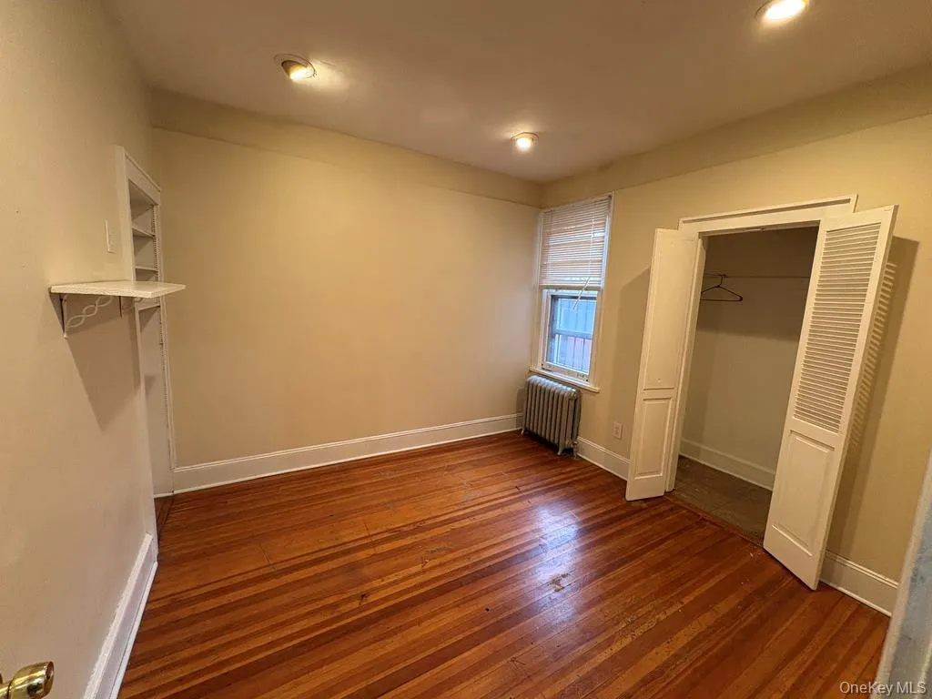 Unfurnished bedroom with dark wood-style floors, radiator heating unit, and a spacious closet Unfurnished bedroom with dark wood-style floors, radiator heating unit, and a spacious closet
