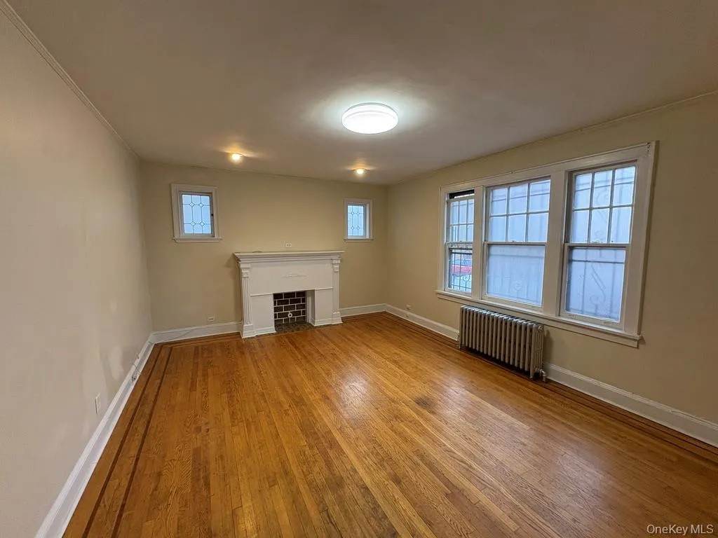Unfurnished living room with radiator, light wood-type flooring, a fireplace, and ornamental molding Unfurnished living room with radiator, light wood-type flooring, a fireplace, and ornamental molding