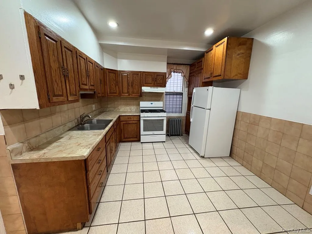 Kitchen featuring light countertops, white appliances, radiator, under cabinet range hood, and tile walls Kitchen featuring light countertops, white appliances, radiator, under cabinet range hood, and tile walls