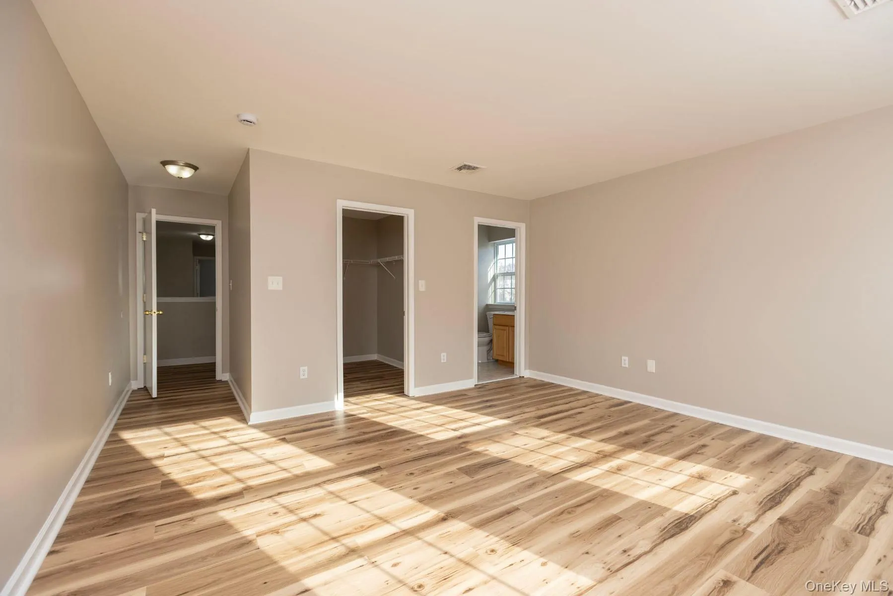 Unfurnished bedroom featuring ensuite bathroom, a walk in closet, and light wood-type flooring Unfurnished bedroom featuring ensuite bathroom, a walk in closet, and light wood-type flooring