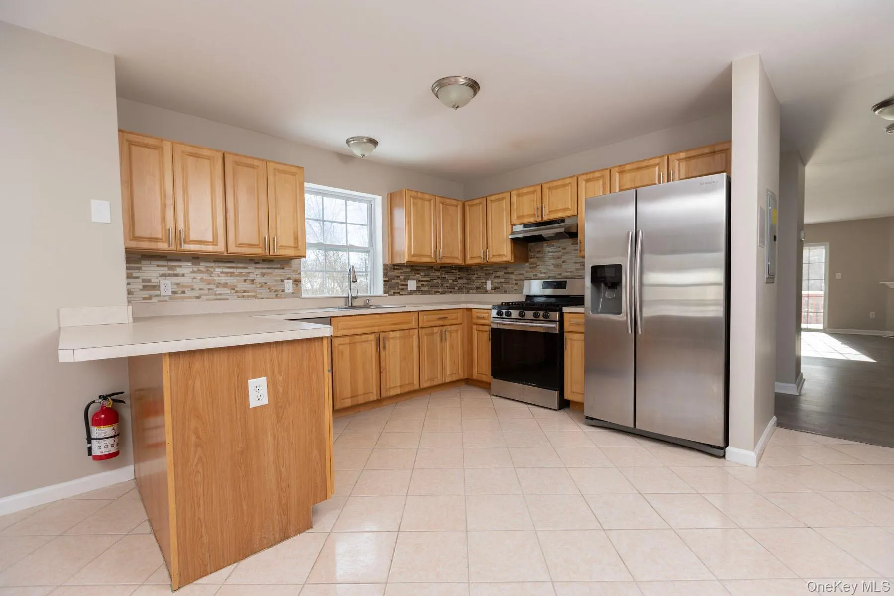 Kitchen featuring light countertops, appliances with stainless steel finishes, backsplash, under cabinet range hood, and light tile patterned floors Kitchen featuring light countertops, appliances with stainless steel finishes, backsplash, under cabinet range hood, and light tile patterned floors