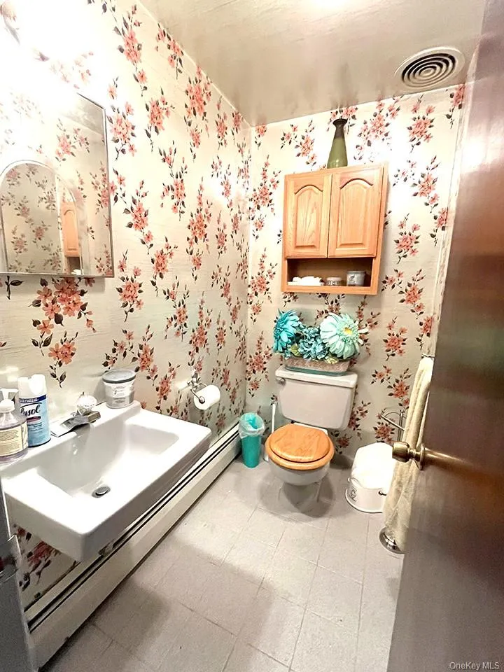 Half bathroom featuring baseboard heating, vanity, and light floors Half bathroom featuring baseboard heating, vanity, and light floors