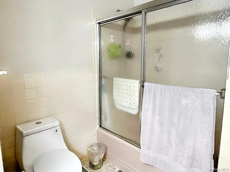 Bathroom with tile walls, a wainscoted wall, and bath / shower combo with glass door Bathroom with tile walls, a wainscoted wall, and bath / shower combo with glass door