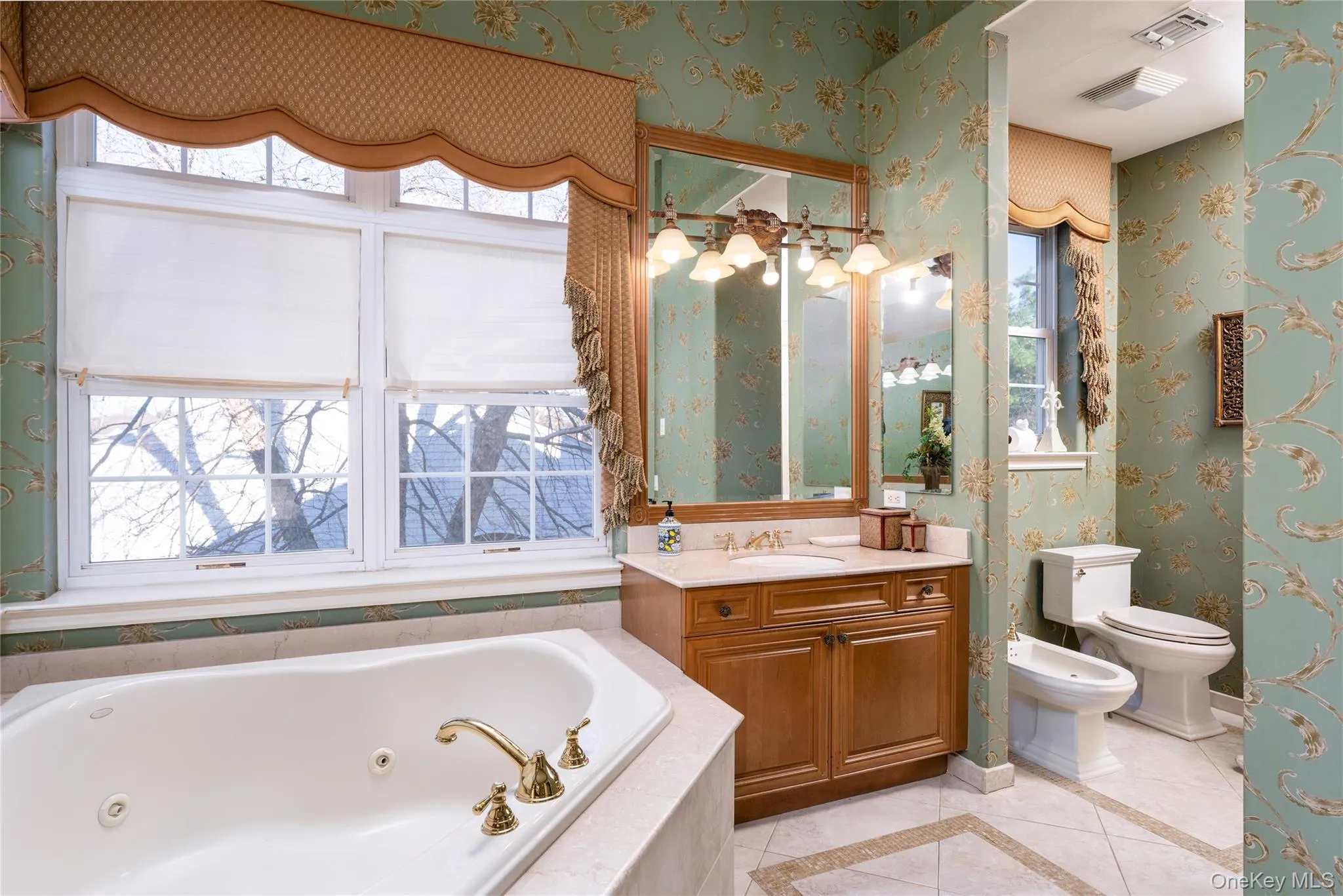 Full bathroom with wallpapered walls, inlaid floor details, a jetted tub, vanity, and light tile patterned flooring Full bathroom with wallpapered walls, inlaid floor details, a jetted tub, vanity, and light tile patterned flooring