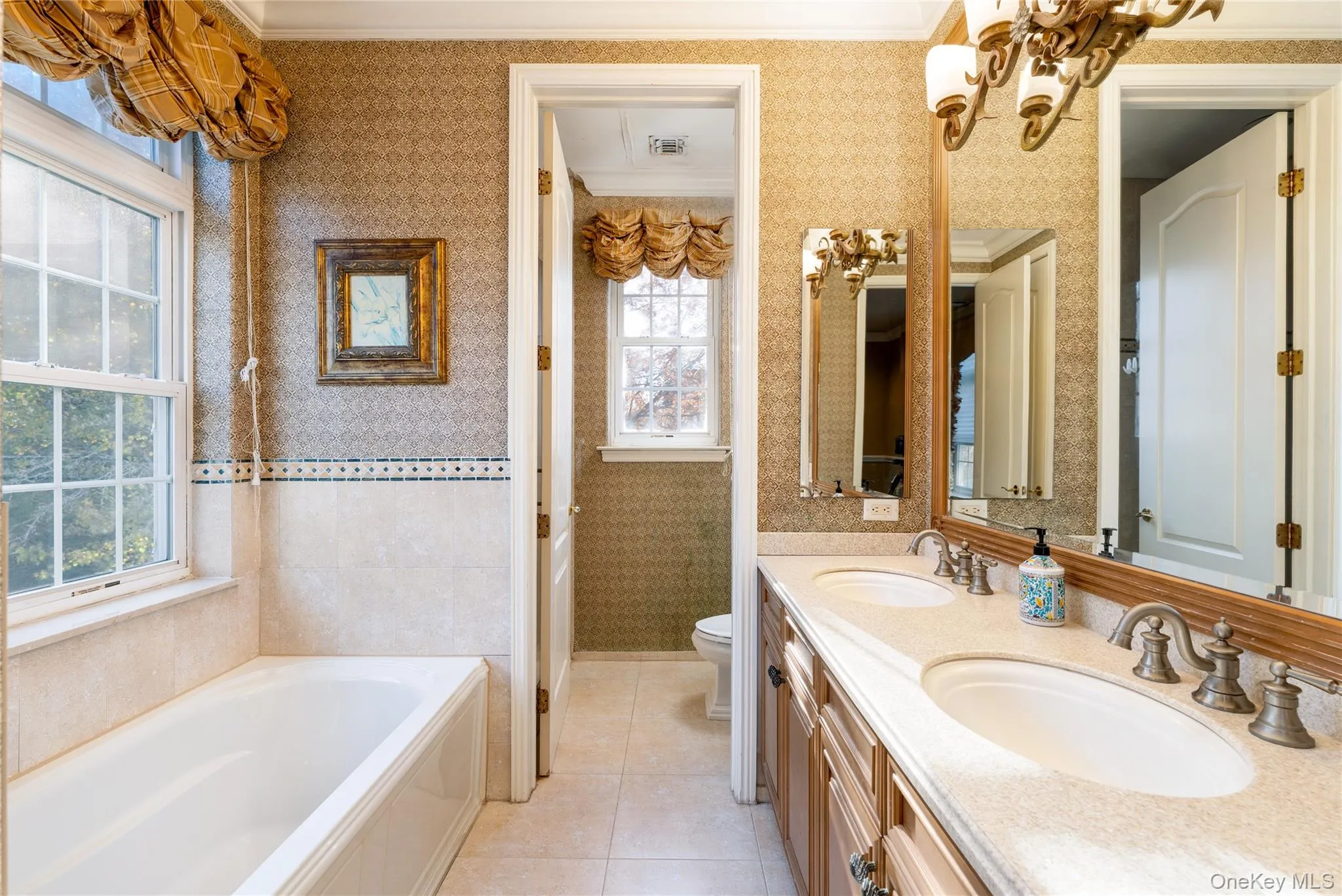 Bathroom featuring wallpapered walls, double vanity, a garden tub, crown molding, and light tile patterned floors Bathroom featuring wallpapered walls, double vanity, a garden tub, crown molding, and light tile patterned floors