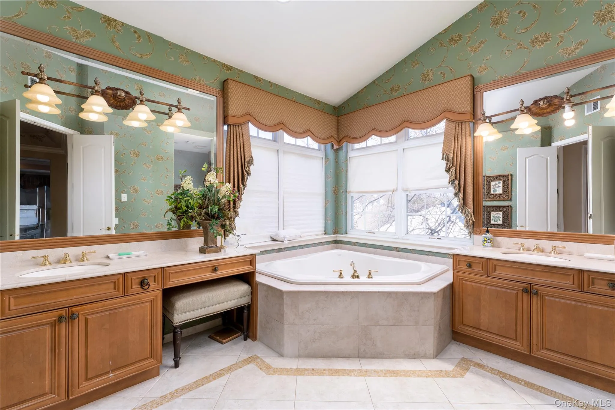 Full bath featuring wallpapered walls, vaulted ceiling, two vanities, inlaid floor details, and light tile patterned floors Full bath featuring wallpapered walls, vaulted ceiling, two vanities, inlaid floor details, and light tile patterned floors