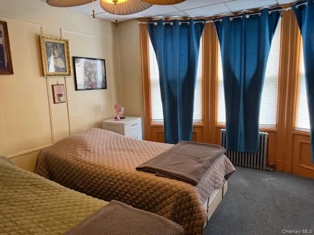 Carpeted bedroom with radiator heating unit and ceiling fan Carpeted bedroom with radiator heating unit and ceiling fan